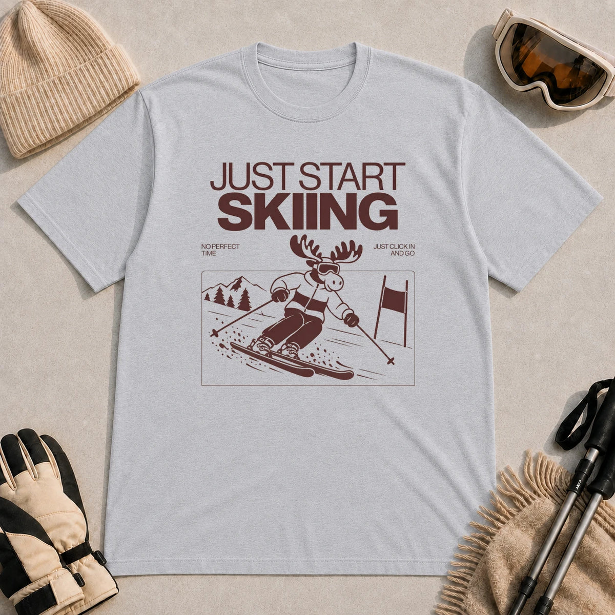 Sport Grey tee featuring a moose skiing through a minimalist mountain scene with the phrases “Just Start Skiing,” “No Perfect Time,” and “Just Click In and Go.”