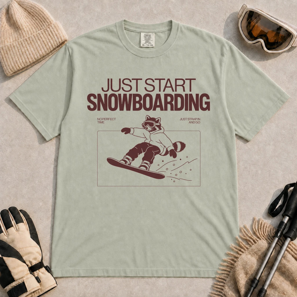 Bay tee featuring a raccoon snowboarding through a minimalist slope scene with the phrases “Just Start Snowboarding,” “No Perfect Time,” and “Just Strap In and Go.”