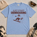Washed Denim tee featuring a raccoon snowboarding through a minimalist slope scene with the phrases “Just Start Snowboarding,” “No Perfect Time,” and “Just Strap In and Go.”
