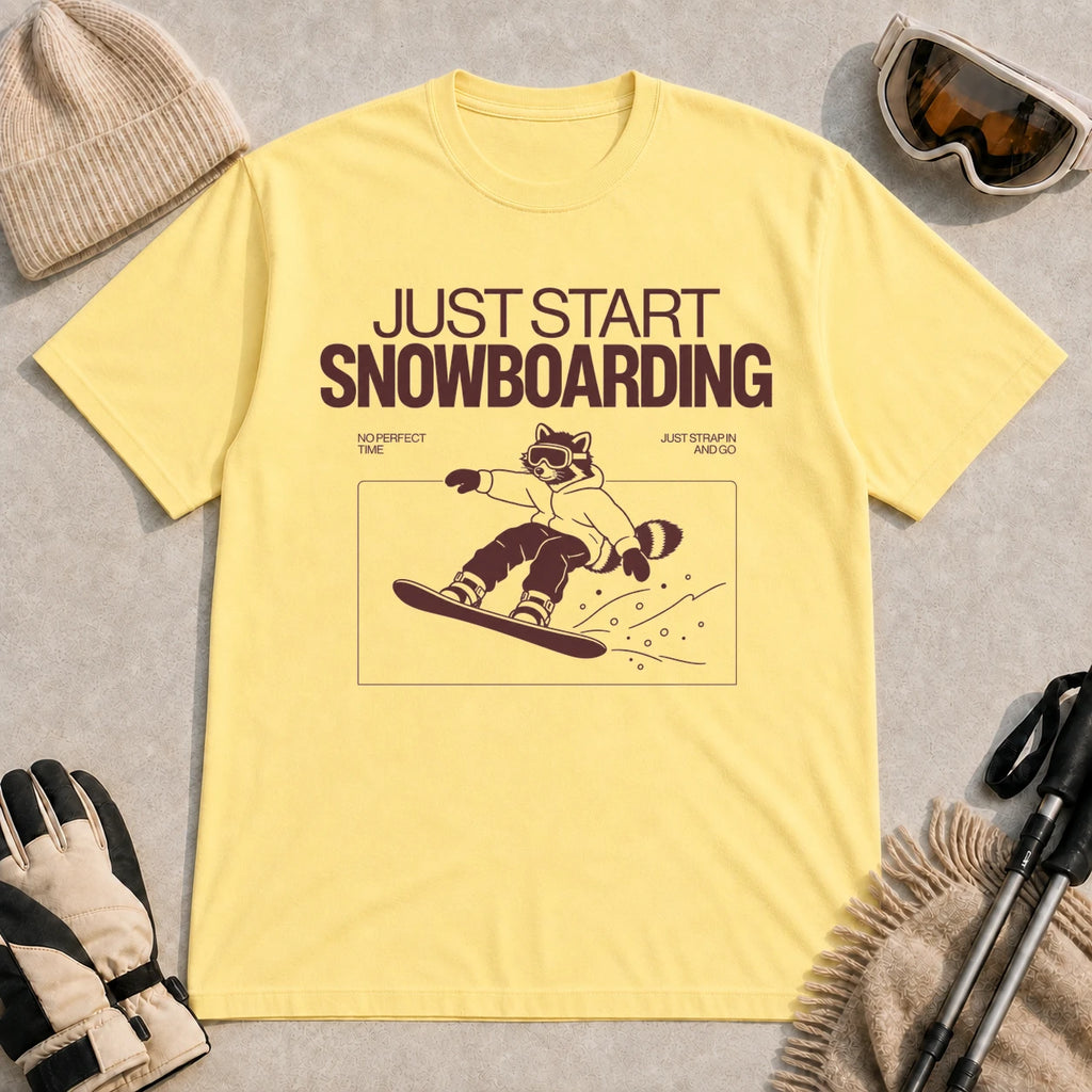 Cornsilk tee featuring a raccoon snowboarding through a minimalist slope scene with the phrases “Just Start Snowboarding,” “No Perfect Time,” and “Just Strap In and Go.”