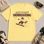 Cornsilk tee featuring a raccoon snowboarding through a minimalist slope scene with the phrases “Just Start Snowboarding,” “No Perfect Time,” and “Just Strap In and Go.”