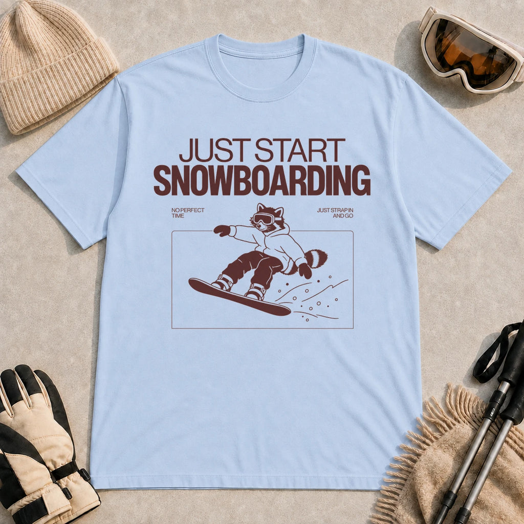 Light Blue tee featuring a raccoon snowboarding through a minimalist slope scene with the phrases “Just Start Snowboarding,” “No Perfect Time,” and “Just Strap In and Go.”