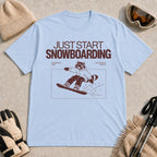 Light Blue tee featuring a raccoon snowboarding through a minimalist slope scene with the phrases “Just Start Snowboarding,” “No Perfect Time,” and “Just Strap In and Go.”