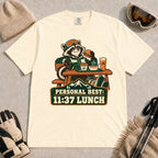 Ivory tee featuring a relaxed raccoon enjoying a burger and fries at a mountain lodge table above the phrase “Personal Best: 11:37 Lunch.”