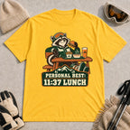 Daisy tee featuring a relaxed raccoon enjoying a burger and fries at a mountain lodge table above the phrase “Personal Best: 11:37 Lunch.”