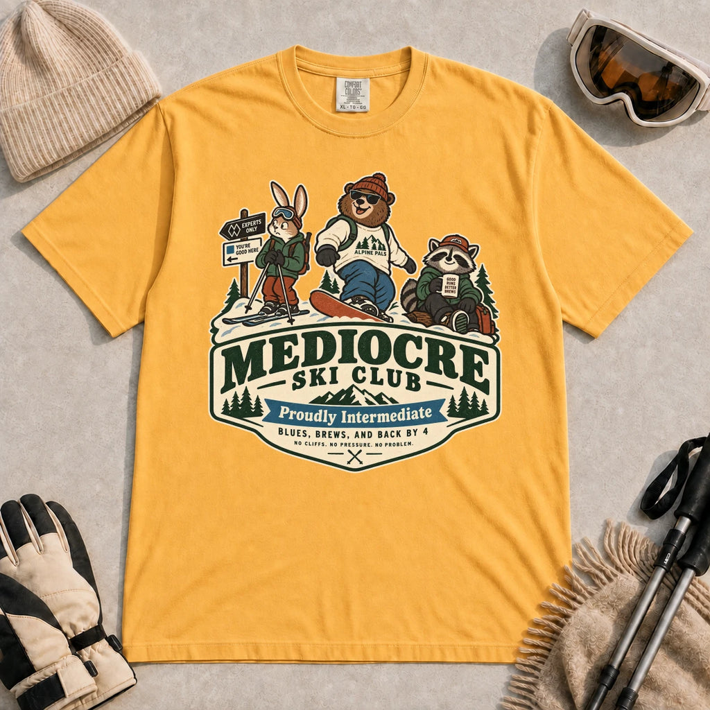 Mustard tee featuring a bear, bunny, and raccoon in ski gear above a retro “Mediocre Ski Club” badge with the phrases “Proudly Intermediate” and “Blues, Brews, and Back by 4.”
