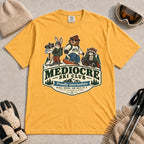 Mustard tee featuring a bear, bunny, and raccoon in ski gear above a retro “Mediocre Ski Club” badge with the phrases “Proudly Intermediate” and “Blues, Brews, and Back by 4.”