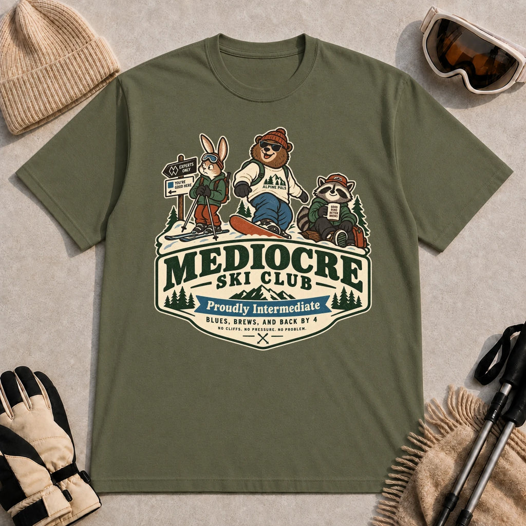 Military Green tee featuring a bear, bunny, and raccoon in ski gear above a retro “Mediocre Ski Club” badge with the phrases “Proudly Intermediate” and “Blues, Brews, and Back by 4.”