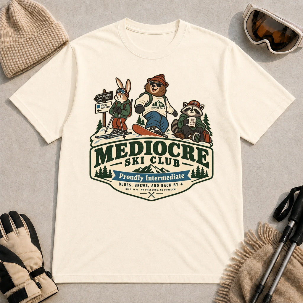 Natural tee featuring a bear, bunny, and raccoon in ski gear above a retro “Mediocre Ski Club” badge with the phrases “Proudly Intermediate” and “Blues, Brews, and Back by 4.”