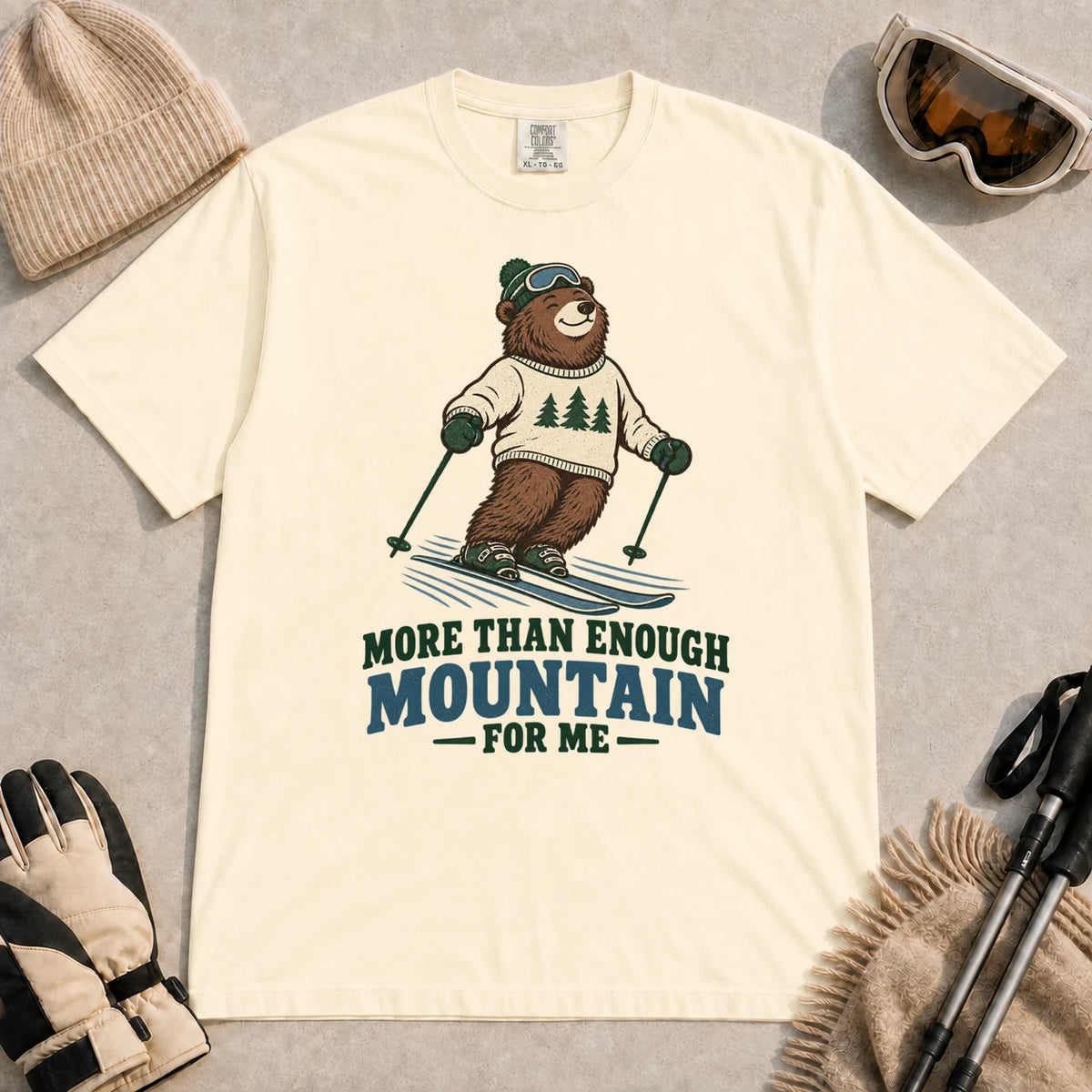 Ivory tee featuring a smiling bear skiing in retro mountain gear above the phrase “More Than Enough Mountain for Me.”