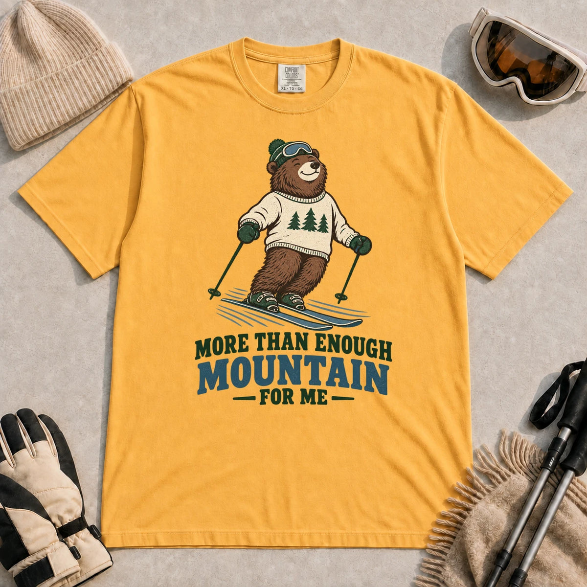 Mustard tee featuring a smiling bear skiing in retro mountain gear above the phrase “More Than Enough Mountain for Me.”