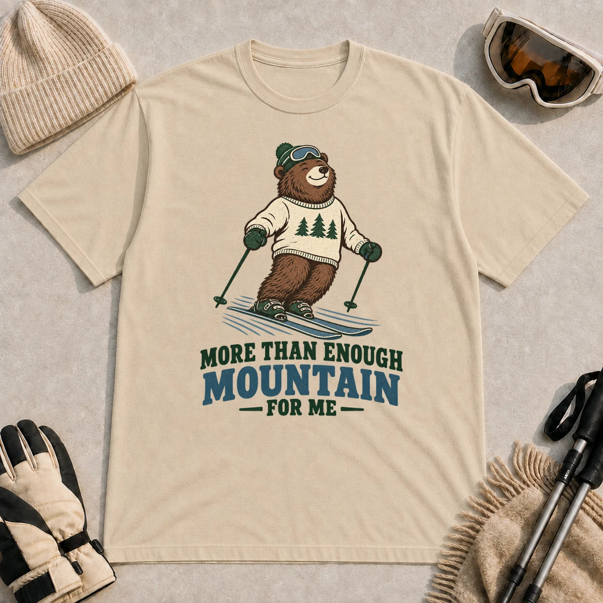 Sand tee featuring a smiling bear skiing in retro mountain gear above the phrase “More Than Enough Mountain for Me.”