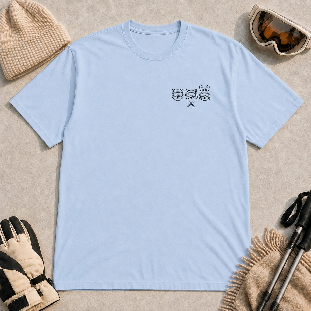 Light Blue tee featuring minimalist black line art of a bear, raccoon, and bunny wearing ski goggles above a small pair of crossed skis.