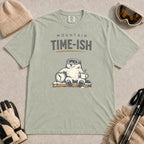 Bay tee featuring a relaxed bear in ski goggles sitting with a steaming mug and clock on a snowy bench, with the phrase “Mountain Time-ish.”