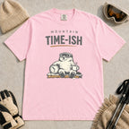 Blossom tee featuring a relaxed bear in ski goggles sitting with a steaming mug and clock on a snowy bench, with the phrase “Mountain Time-ish.”