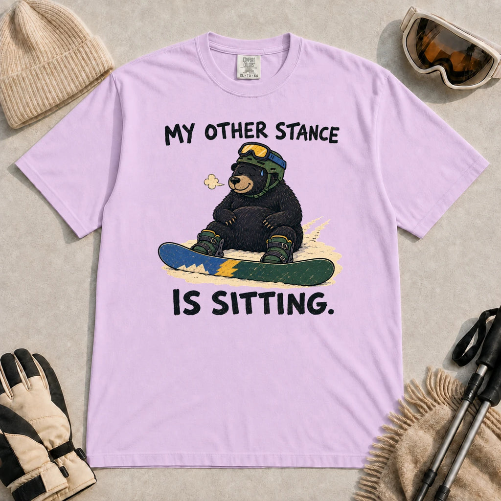 Orchid tee featuring a tired bear sitting on a snowboard in ski gear with the phrase “My Other Stance Is Sitting.”