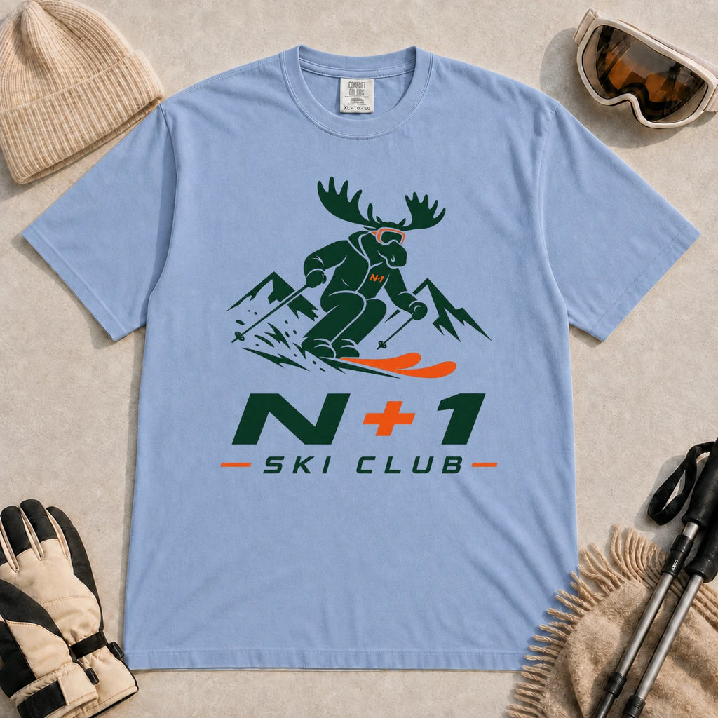 Washed Denim tee featuring a moose skiing through the mountains in a bold green and orange graphic, with the phrase “N+1 Ski Club.”