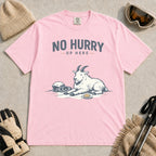 Blossom tee featuring a relaxed mountain goat resting in the snow beside ski goggles and a helmet with the phrase “No Hurry Up Here.”