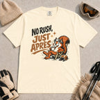 Ivory tee featuring a cheerful squirrel in ski goggles relaxing in a chair with a hot drink and helmet, with the phrase “No Rush, Just Après.”