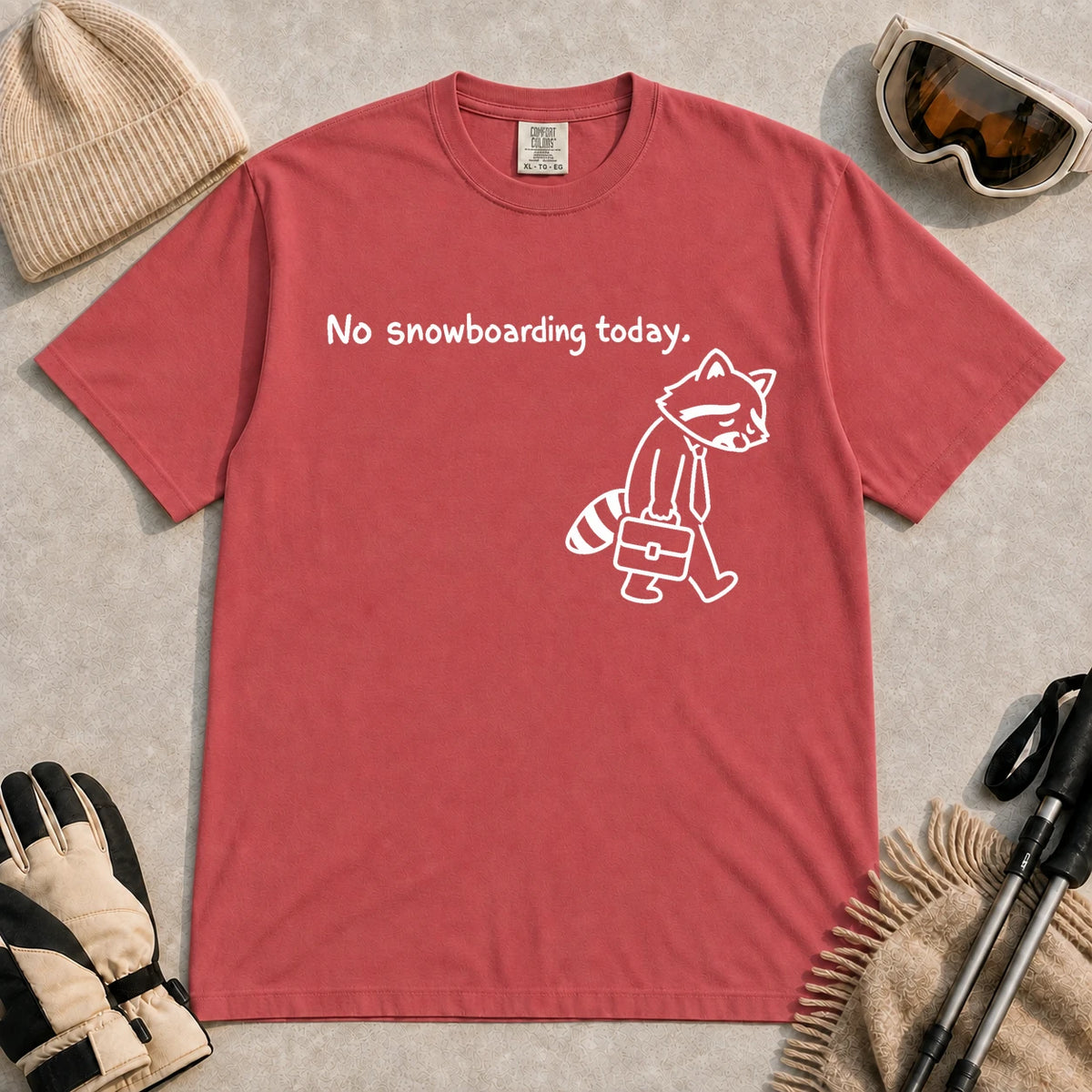 Crimson tee featuring a sad raccoon dressed for work and carrying a briefcase beneath the phrase “No snowboarding today.”
