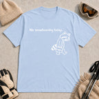 Light Blue tee featuring a sad raccoon dressed for work and carrying a briefcase beneath the phrase “No snowboarding today.”