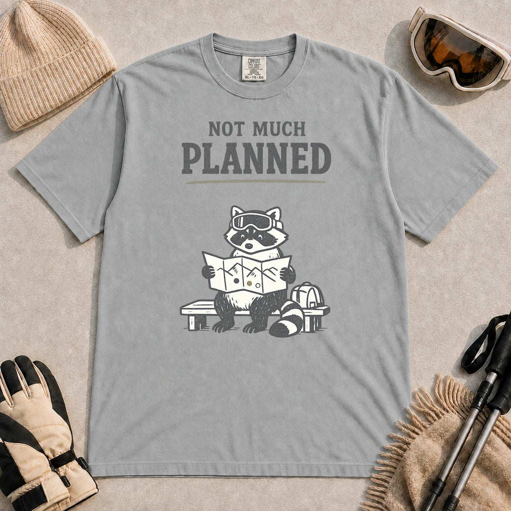 Granite tee featuring a raccoon in ski goggles sitting on a bench and studying a trail map beside a backpack, with the phrase “Not Much Planned.”