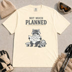 Ivory tee featuring a raccoon in ski goggles sitting on a bench and studying a trail map beside a backpack, with the phrase “Not Much Planned.”