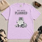 Orchid tee featuring a raccoon in ski goggles sitting on a bench and studying a trail map beside a backpack, with the phrase “Not Much Planned.”