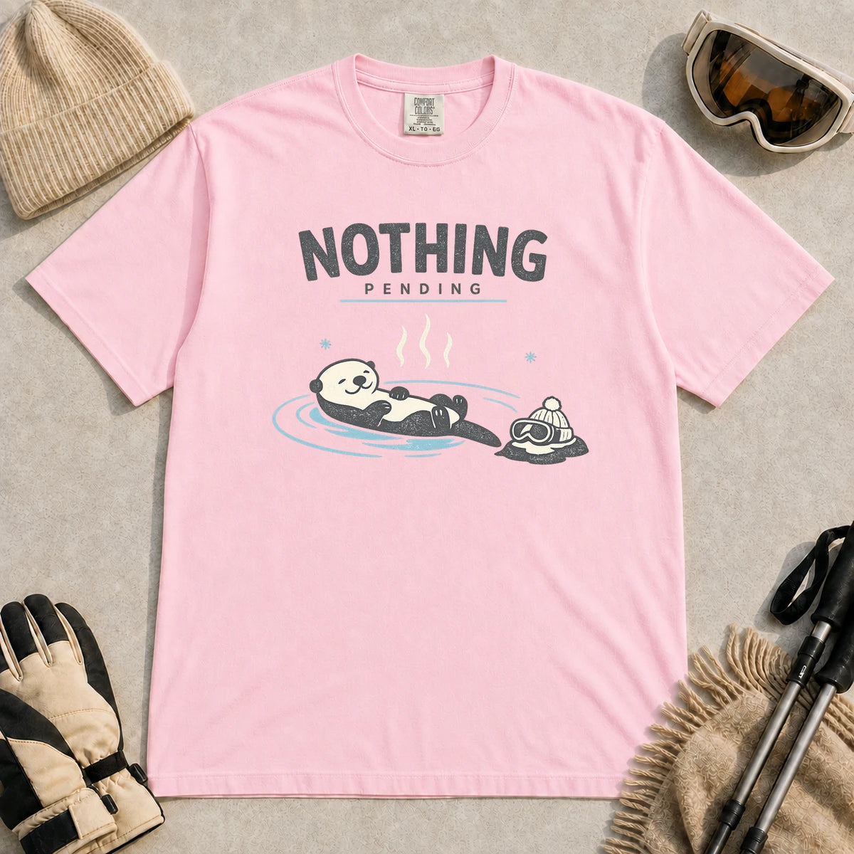 Blossom tee featuring a relaxed otter soaking in a hot spring beside ski goggles and a beanie, with the phrase “Nothing Pending.”