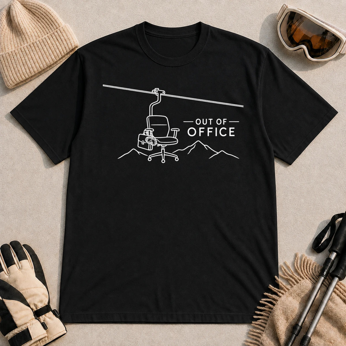Black tee featuring a minimalist white line-art chairlift carrying an office chair above mountain outlines beside the phrase “Out of Office.”