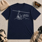 Navy tee featuring a minimalist white line-art chairlift carrying an office chair above mountain outlines beside the phrase “Out of Office.”
