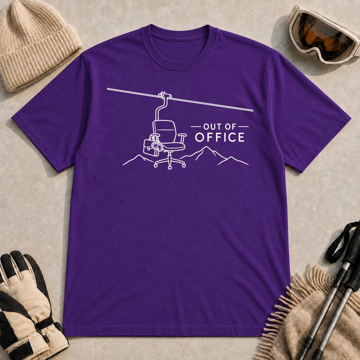 Purple tee featuring a minimalist white line-art chairlift carrying an office chair above mountain outlines beside the phrase “Out of Office.”