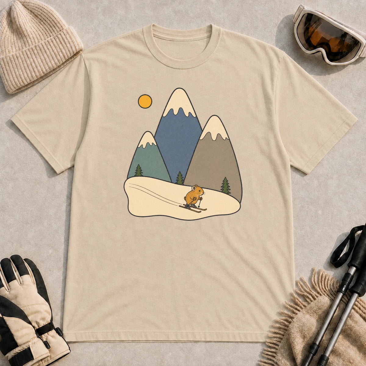 Sand tee featuring a minimalist alpine scene with a tiny pika skiing beneath three snowcapped mountain peaks and a golden sun.
