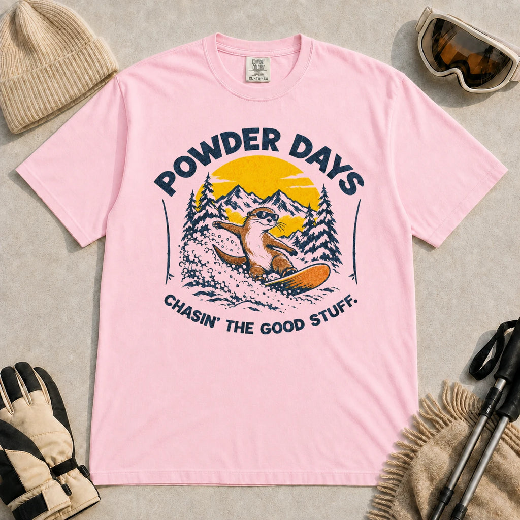 Blossom tee featuring a sunglasses-wearing otter snowboarding through powder beneath a mountain sunset, with the phrases “Powder Days” and “Chasin’ the Good Stuff.”