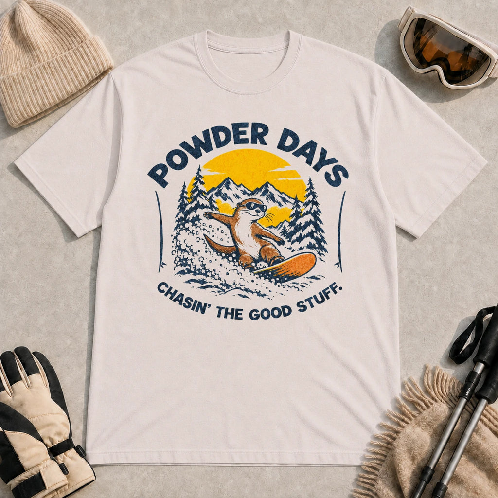 Ice Grey tee featuring a sunglasses-wearing otter snowboarding through powder beneath a mountain sunset, with the phrases “Powder Days” and “Chasin’ the Good Stuff.”