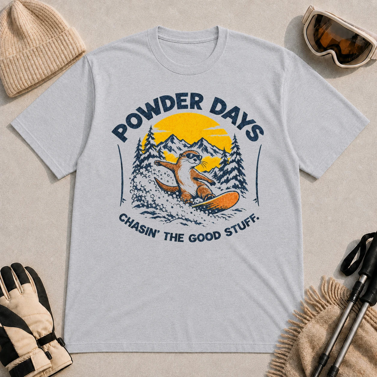 Sport Grey tee featuring a sunglasses-wearing otter snowboarding through powder beneath a mountain sunset, with the phrases “Powder Days” and “Chasin’ the Good Stuff.”