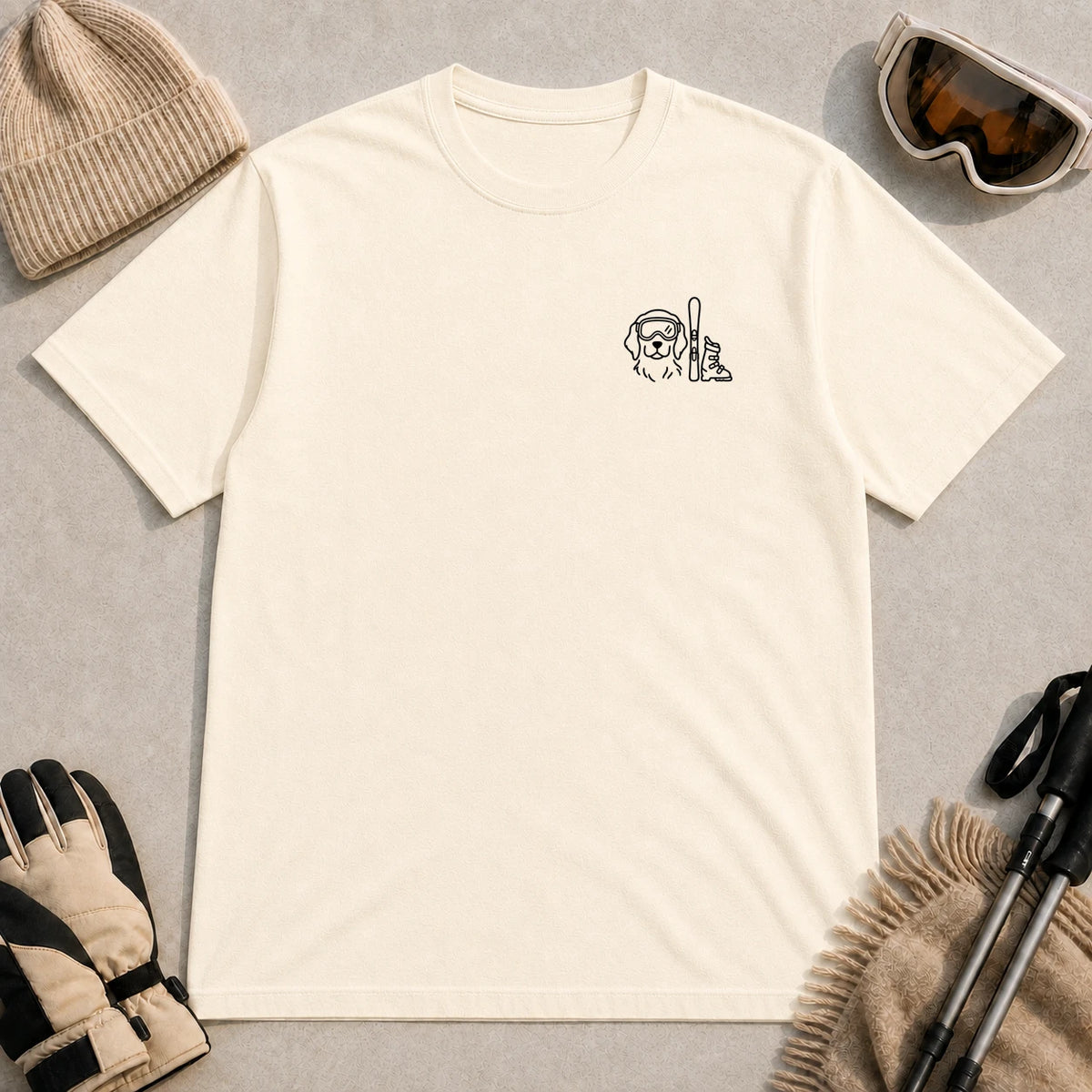 Natural tee featuring minimalist black line art of a goggle-wearing dog beside an upright ski and ski boot.