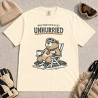 Ivory tee featuring a relaxed beaver in ski goggles sitting in a chair with a hot drink, with the phrase “Professionally Unhurried.”