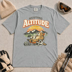 Granite tee featuring a relaxed marmot lounging in a chair with a hot drink beside ski goggles, backed by mountains and a retro sunset with the phrase “Resting Altitude.”