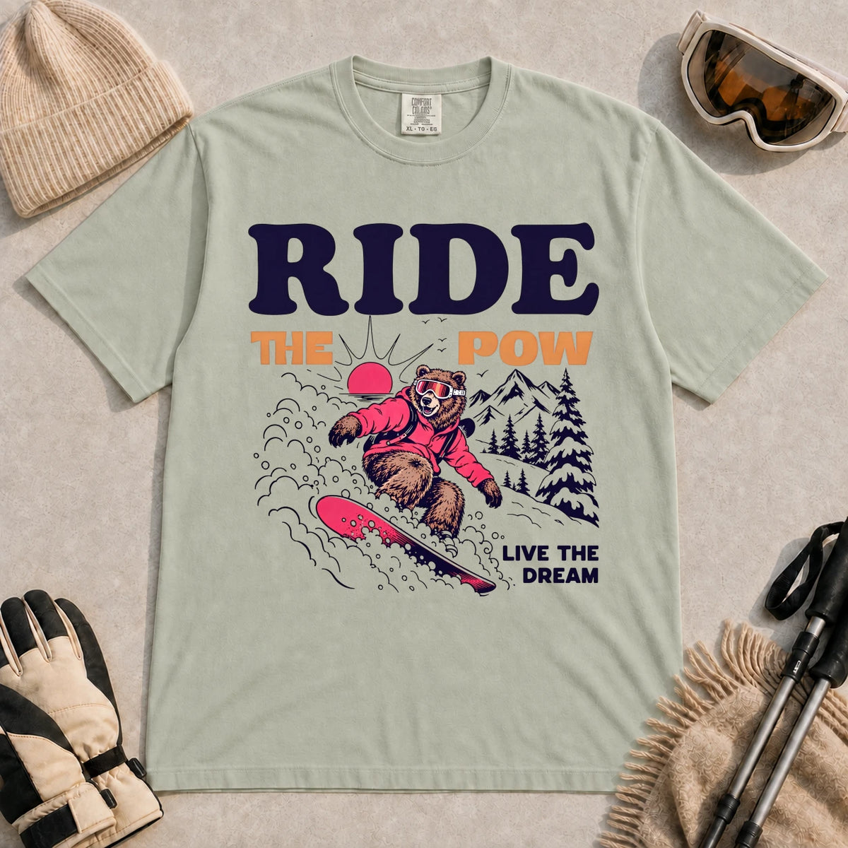 Bay tee featuring a bear snowboarding through powder in a retro mountain scene with the phrases “Ride the Pow” and “Live the Dream.”