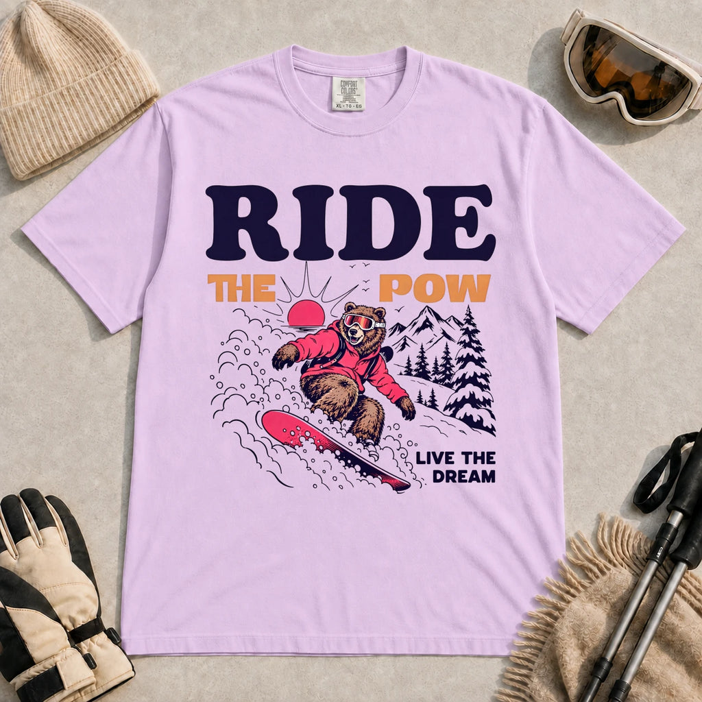 Orchid tee featuring a bear snowboarding through powder in a retro mountain scene with the phrases “Ride the Pow” and “Live the Dream.”
