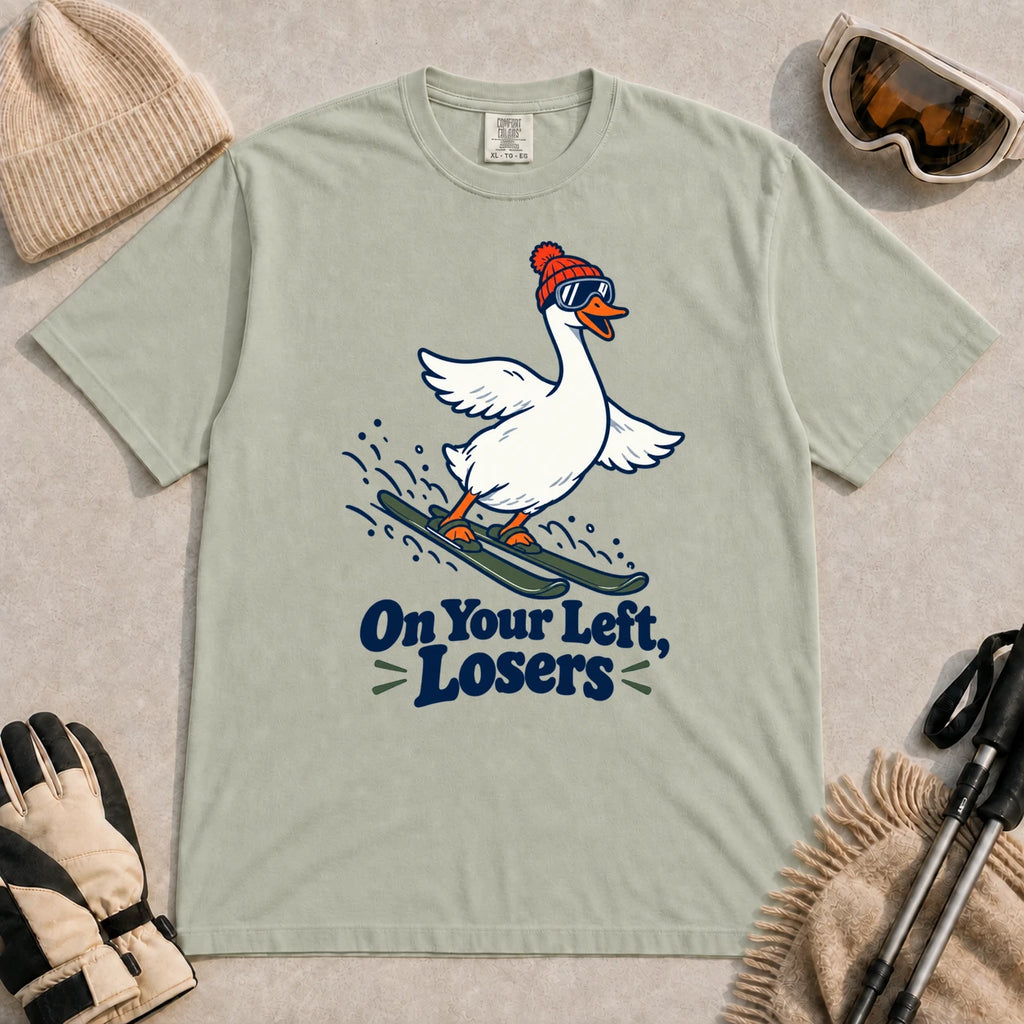 Bay tee featuring a playful goose skiing in goggles and a beanie above the phrase “On Your Left, Losers.”