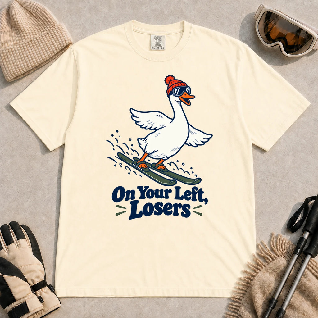 Ivory tee featuring a playful goose skiing in goggles and a beanie above the phrase “On Your Left, Losers.”