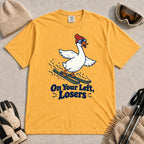 Mustard tee featuring a playful goose skiing in goggles and a beanie above the phrase “On Your Left, Losers.”