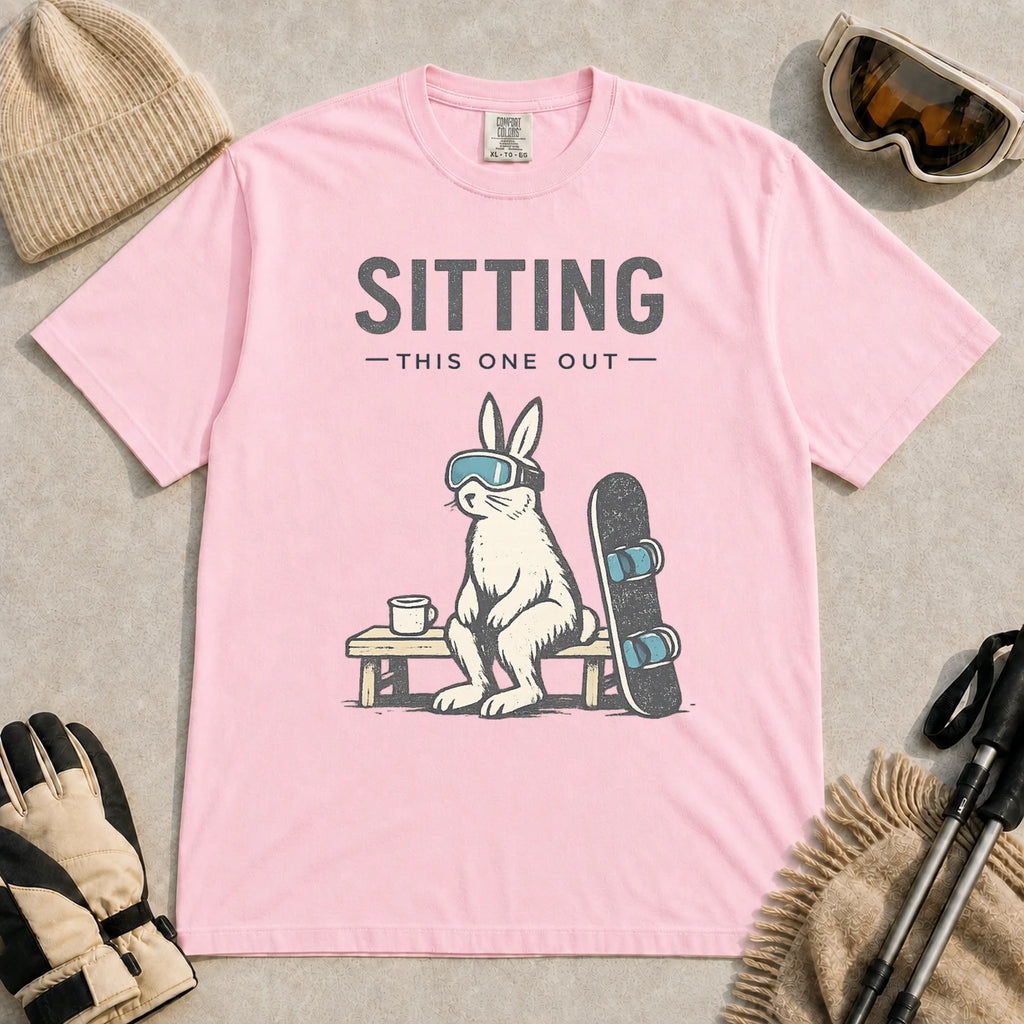 Blossom tee featuring a bunny in ski goggles sitting on a bench beside a snowboard and hot drink with the phrase “Sitting This One Out.”