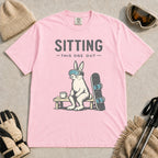 Blossom tee featuring a bunny in ski goggles sitting on a bench beside a snowboard and hot drink with the phrase “Sitting This One Out.”