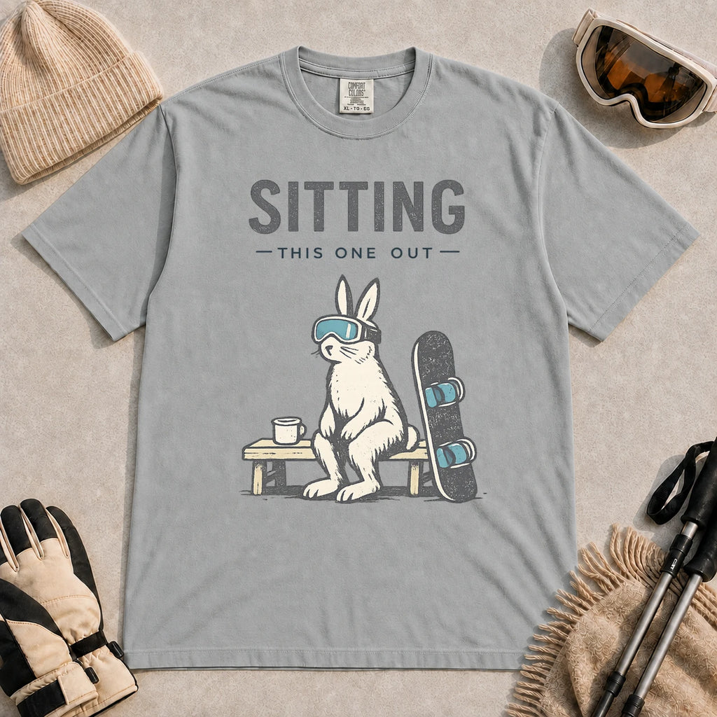 Granite tee featuring a bunny in ski goggles sitting on a bench beside a snowboard and hot drink with the phrase “Sitting This One Out.”