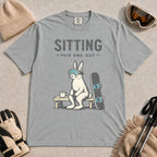 Granite tee featuring a bunny in ski goggles sitting on a bench beside a snowboard and hot drink with the phrase “Sitting This One Out.”
