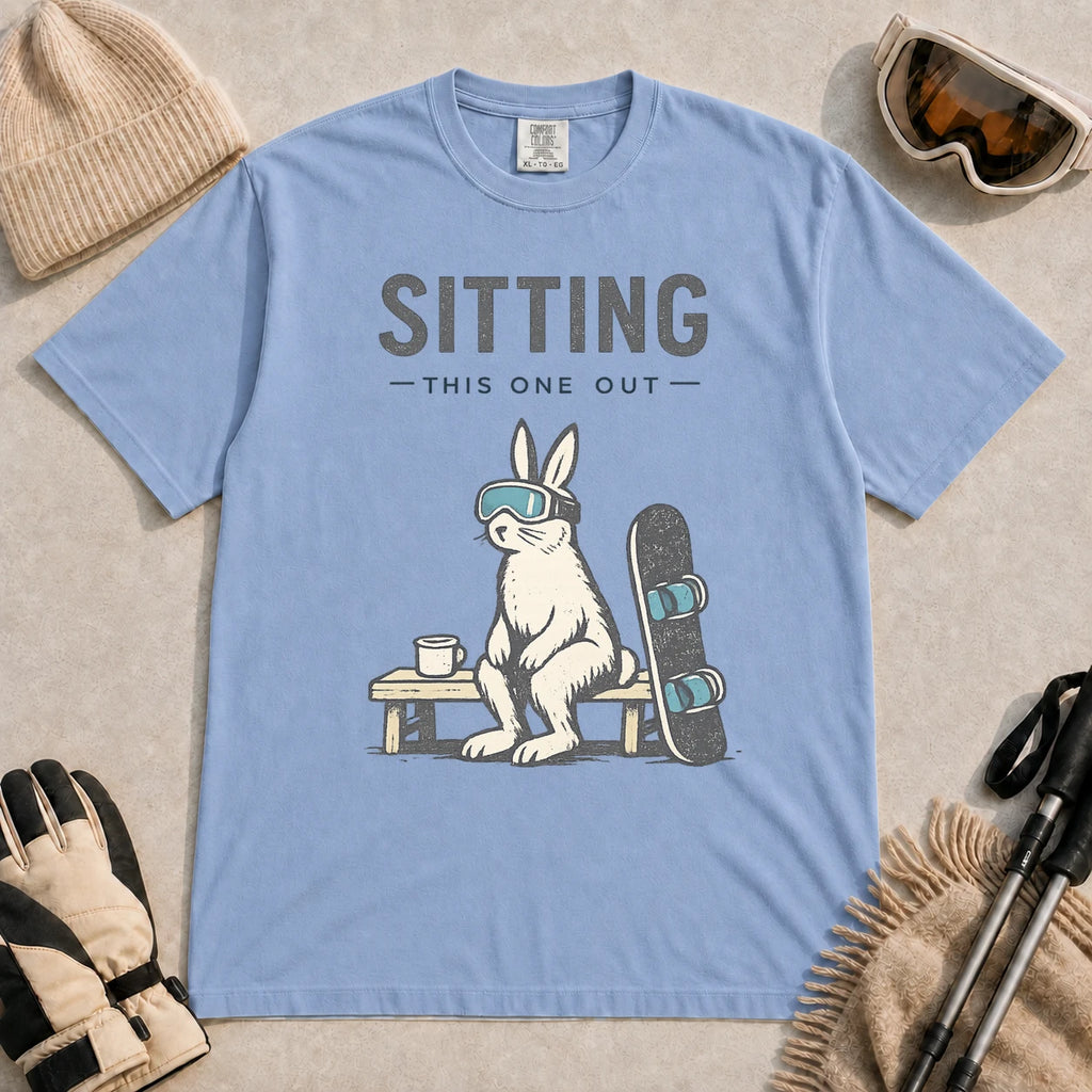 Washed Denim tee featuring a bunny in ski goggles sitting on a bench beside a snowboard and hot drink with the phrase “Sitting This One Out.”