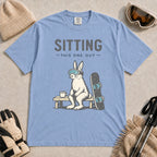 Washed Denim tee featuring a bunny in ski goggles sitting on a bench beside a snowboard and hot drink with the phrase “Sitting This One Out.”